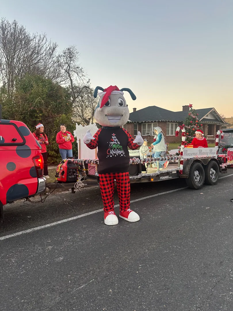 Johnnie the Spot On mascot beside the company's decorated Christmas parade float