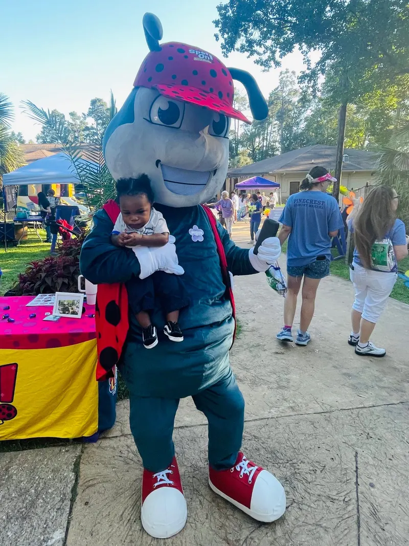 Johnnie on the Spot, the Spot On Pest Control ladybug mascot, holding a child at a community walk