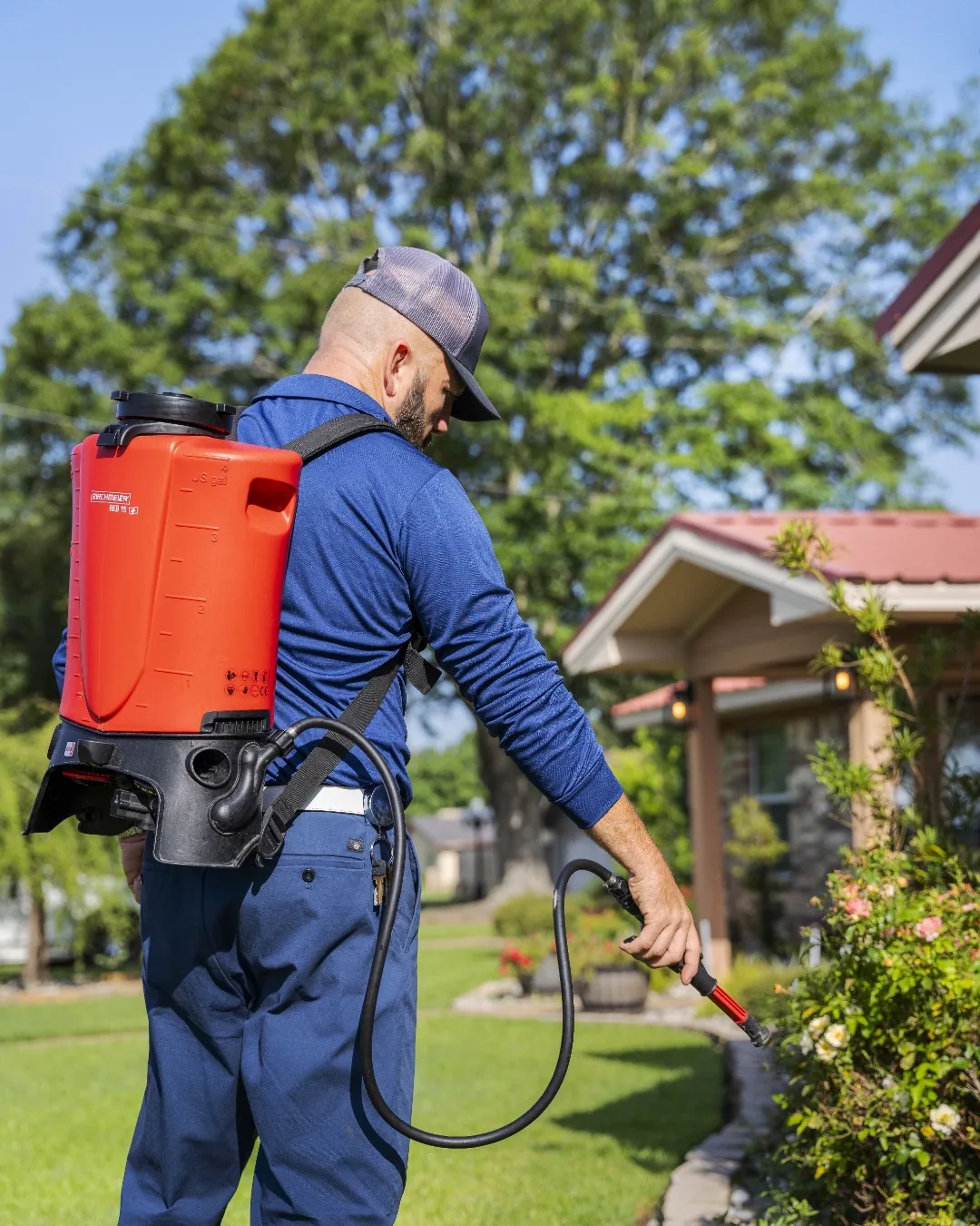 A Spot On technician treating the exterior foundation of an East Texas home with a backpack sprayer