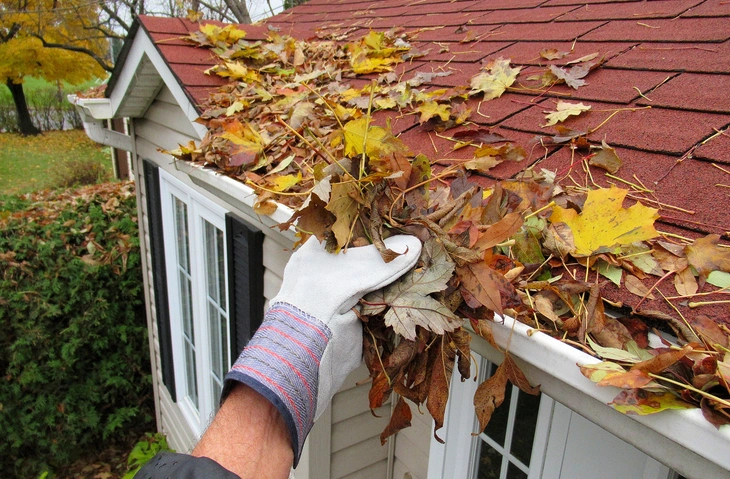 Gutter Cleaning in Lufkin, TX 1 A person cleaning leaves off a roof with a broom on a sunny day.