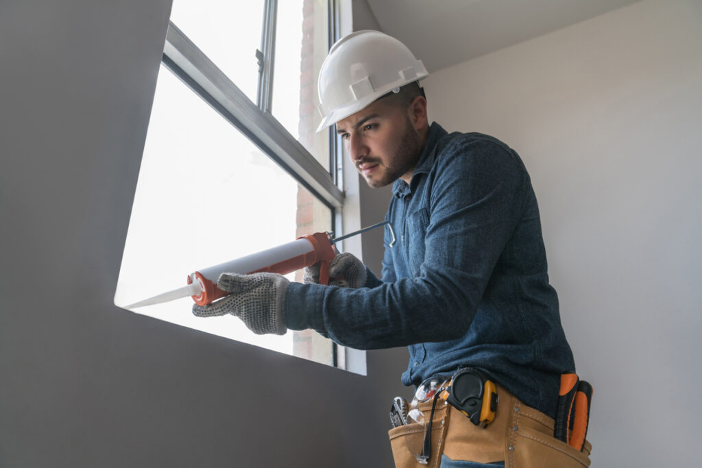 Window Sealing in Lufkin, TX 1 A man in a hard hat repairs a window using a tool, focusing on sealing it properly.